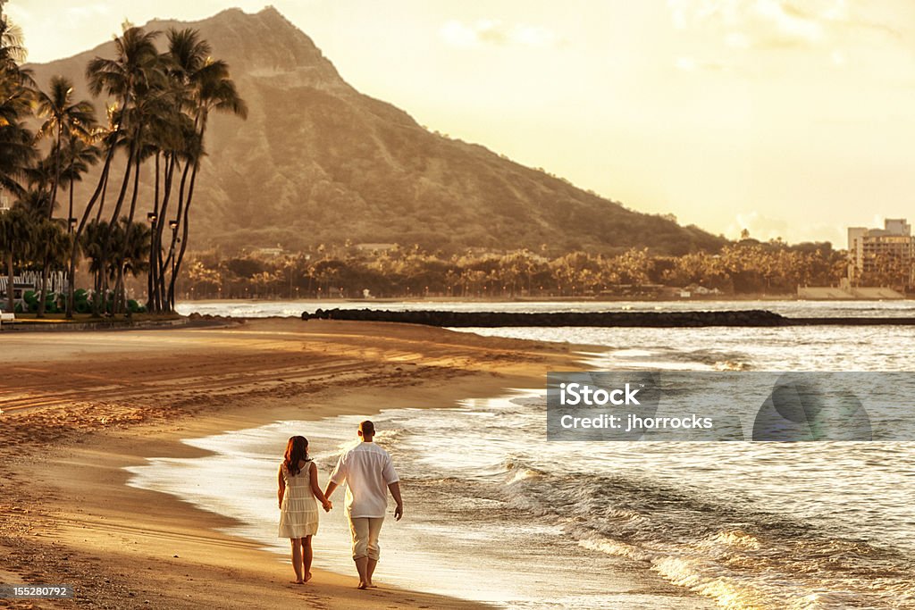 Happy Couple Walking on Waikiki Beach at Sunrise Photo of a happy young couple walking hand-in-hand on Waikiki beach at sunrise. Big Island - Hawaii Islands Stock Photo