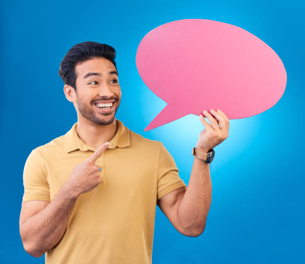 istock Pointing, speech bubble and thinking Asian man for communication, feedback or chat. Excited, talk and a person with a board for conversation isolated on a blue background in a studio with space 1552816567