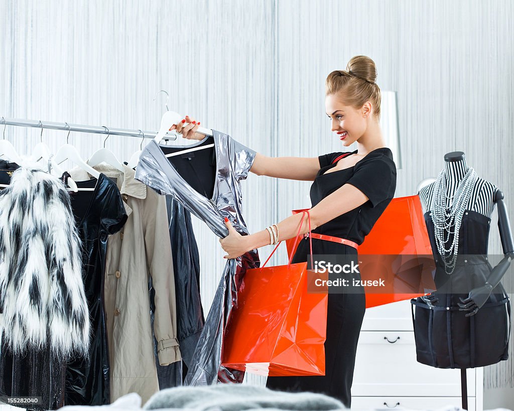 Beautiful woman shopping Beautiful young adult woman shopping in luxury boutique, looking at silver dress and smiling. 20-24 Years Stock Photo