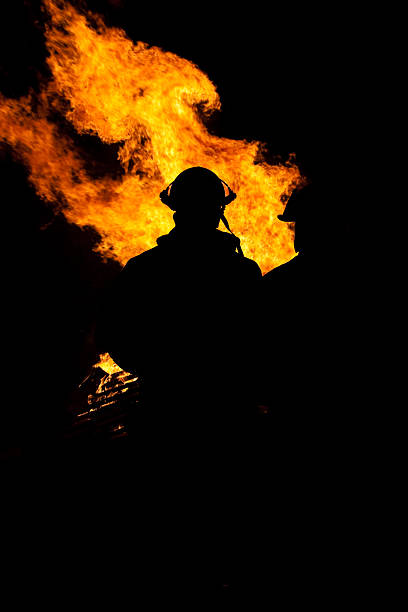 silhouette of  firemen with flames in background stock photo