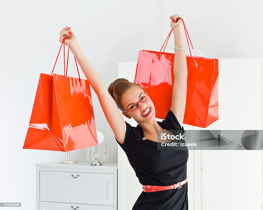 I love shopping! Excited young adult elegant woman holding up red shopping bags and smiling at the camera. Black Color Stock Photo