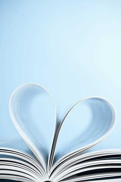 Love to read, pages folded into heart shape, blue background Book pages folded into a heart shape on powder blue background. Copy space, vertical, studio shot. book heart shape valentines day copy space stock pictures, royalty-free photos & images