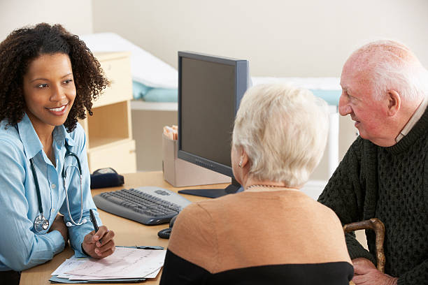 A young, black nurse talking to an elderly couple Smiling young female Doctor talking to senior couple. english spoken stock pictures, royalty-free photos & images