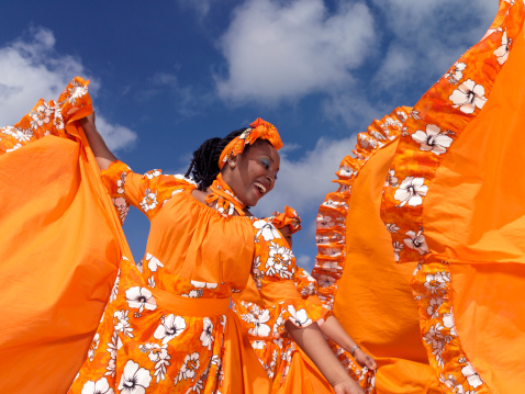 Caribbean dancing troupe wearing bright orange costumes perform on a beach.