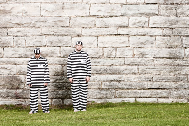 Two Inmates Stand in Front of Prison Wall