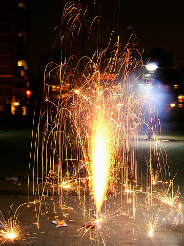 Happy New Year! Friends celebrating with burning sparklers in hands against christmas tree lights in dark room. Hands holding fireworks on background of stylish decorated illuminated tree. Moody