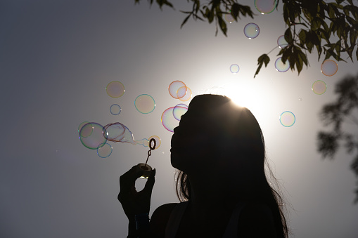 Young woman is playing with bubble wand at sunset.