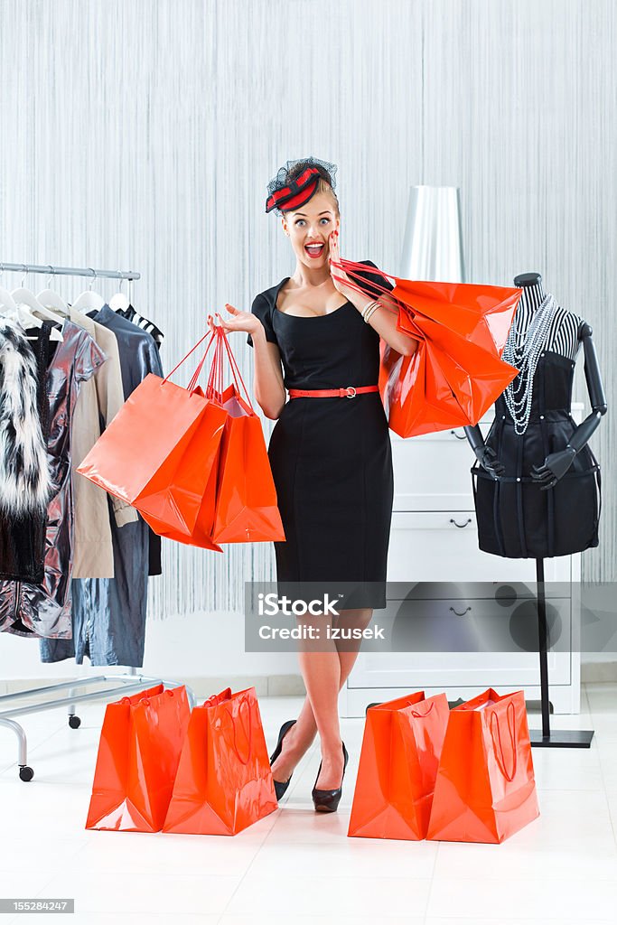 Beautiful shopaholic Elegant and happy young adult woman posing with many shopping bags in luxury boutique. Retail Stock Photo