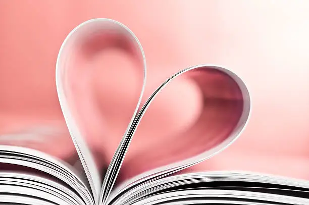 Love to read, close-up of pages folded into heart shape, isolated on pink background. Studio shot.