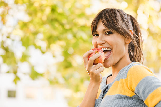 Cheerful young woman eating an apple Outdoors portrait of a pretty girl apple bite stock pictures, royalty-free photos & images