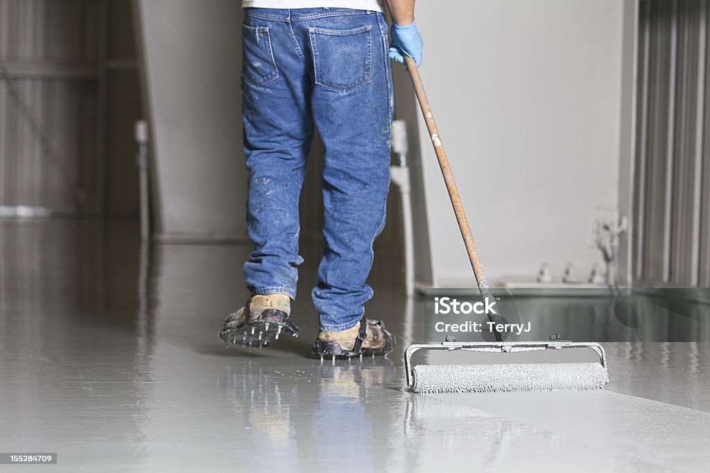 Floor Painting A man pulls a paint roller across a warehouse floor. Epoxy Stock Photo