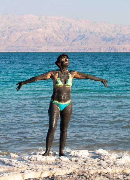 A woman covered in mineral-rich mud at the Dead Sea shore.