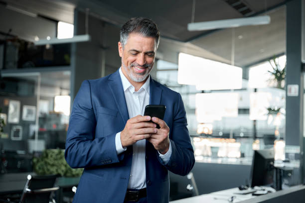 istock Happy middle-aged business man wearing suit using smartphone in office. 1552851604