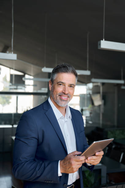 istock Happy middle aged business man wearing suit in office using digital tablet. 1552851616