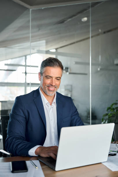 istock Happy middle aged business man ceo wearing suit sitting in office using laptop. 1552851633