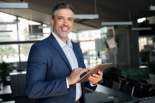 istock Happy middle aged business man wearing suit using digital tablet in office. 1552851640