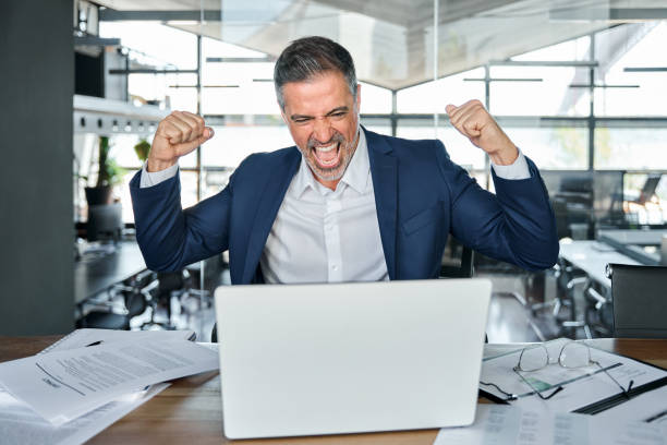 istock Happy mature business man looking at computer feeling euphoria about online win. 1552851647