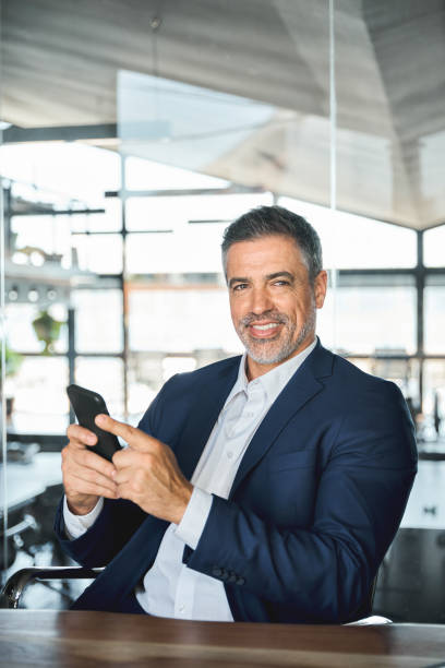 istock Mid aged happy successful business man using mobile phone in office, vertical. 1552851852