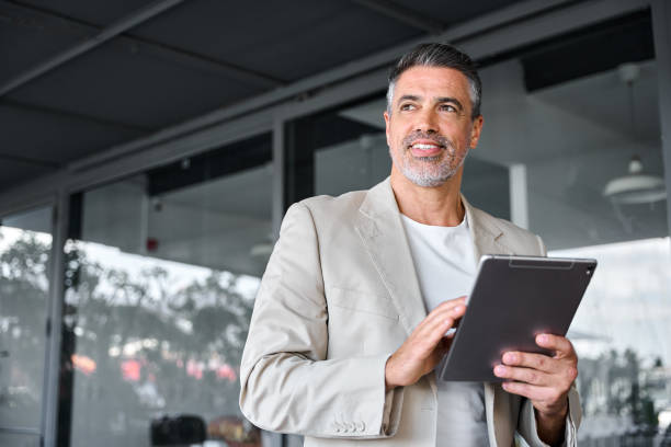 istock Smiling mid aged business man standing outside office holding digital tablet. 1552852723