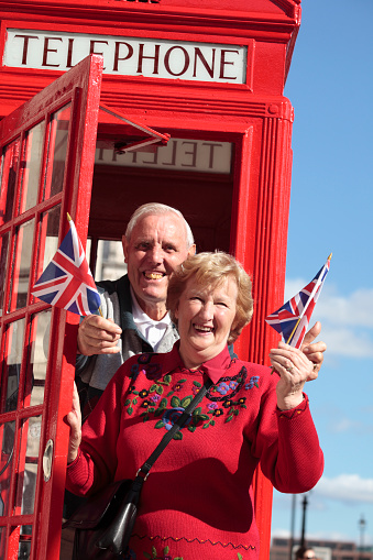 Senior couple holding British flag in London with traditional telephone box. Big Ben in the background.