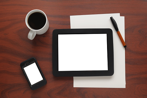 Top view digital tablet with white screen, glasses, coffee cup and camera on wooden table.