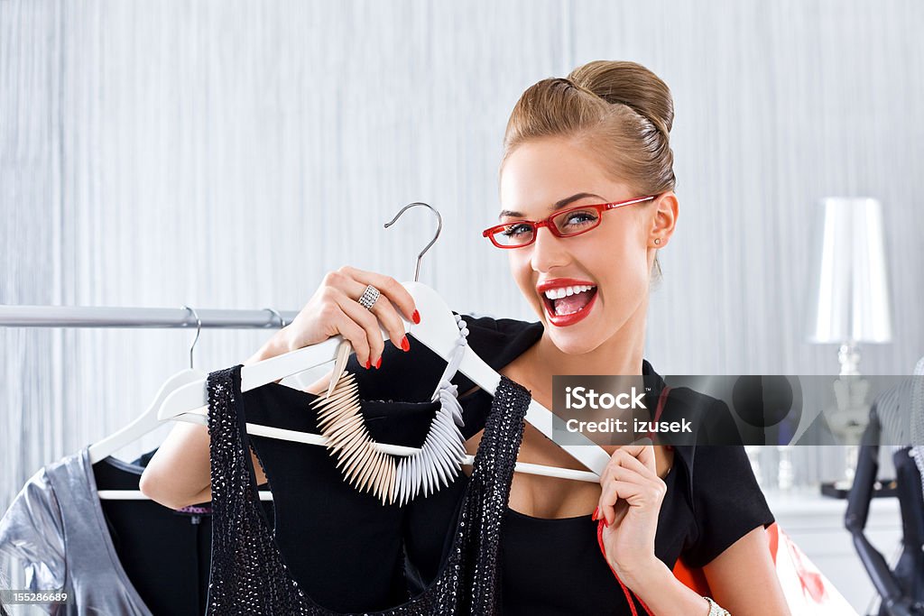 Happy woman during shopping Happy young adult woman shopping in luxury boutique, showing black dress to the camera. 20-24 Years Stock Photo