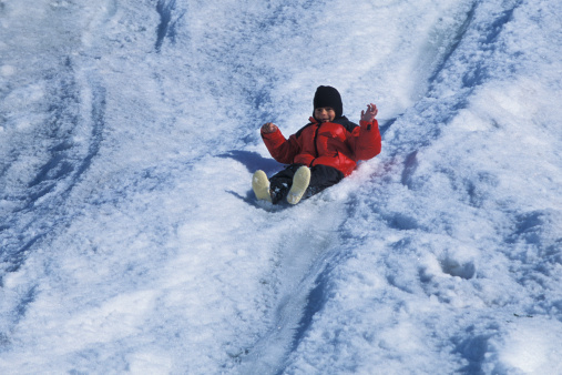 One young latino boy, in red jacket, sliding down snow chute.