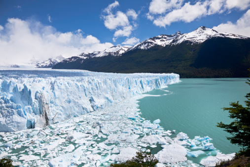 An ice stack the height of a tall building has just fallen into the lake, causing a ring of ice to form at it's base.