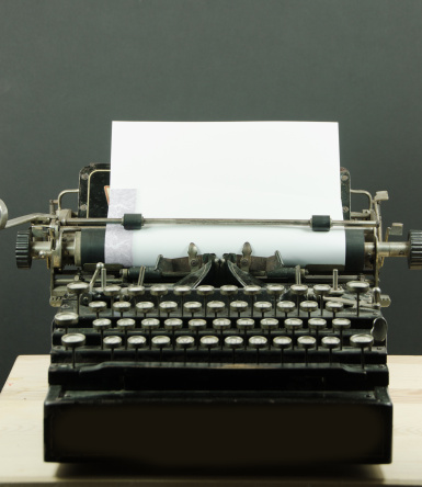 A close-up of a very old and worn typewriter with linen paper for copy space. Black background and full frontal view.