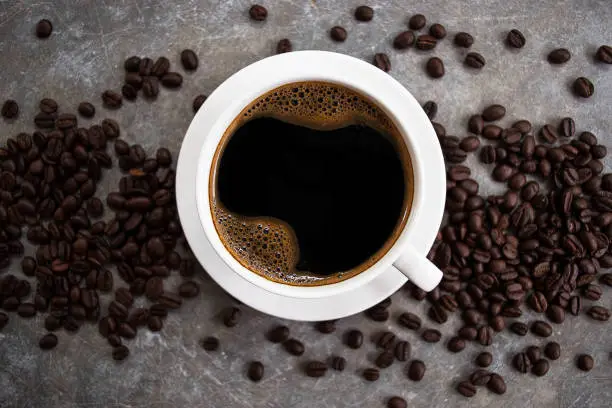 Photo of Black coffee in a white glass placed on an old cement table with coffee beans.