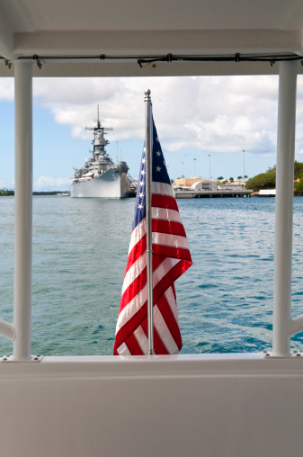 An American flag with the USS Missouri in the background. Located in Pearl Harbor, Hawaii, this Iowa class battleship is perhaps most famous for hosting the signing ceremony for the Japanese surrender at the end of World War II in September 1945. Today it is a museum ship in Pearl Harbor. Photo taken from aboard a ferry docked at the USS Arizona Memorial