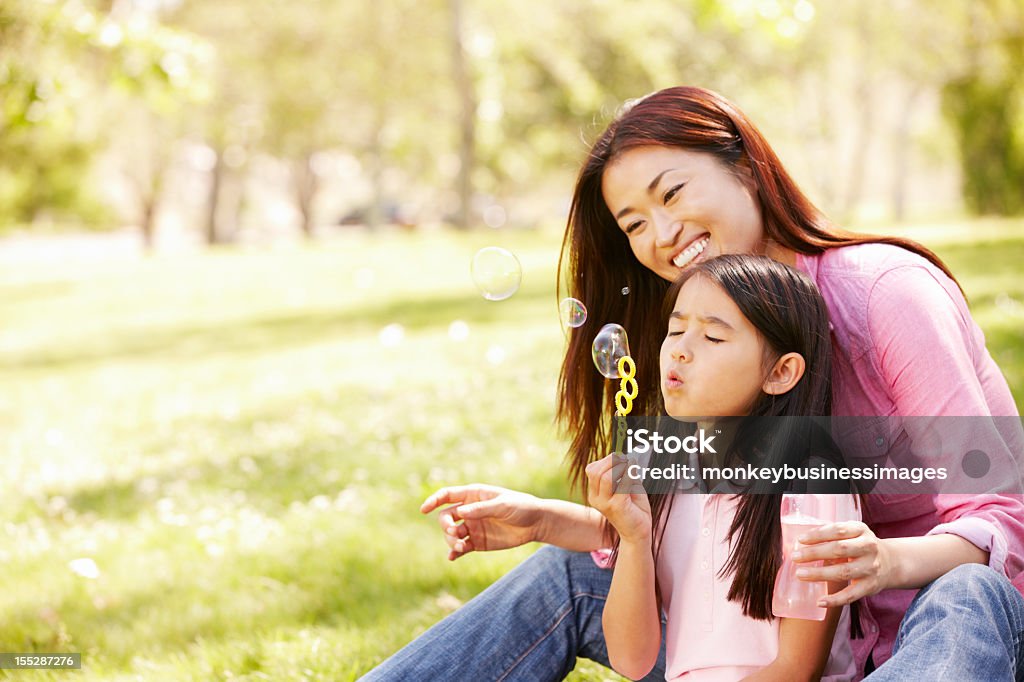 Asiático Soplando burbujas Madre e hija en el parque - Foto de stock de Familia libre de derechos