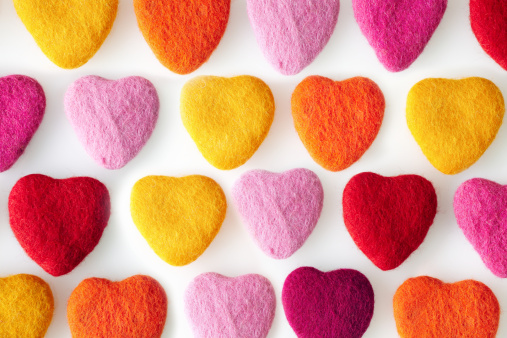 Rows of colorful felt shaped hearts made from wool felt on a white background