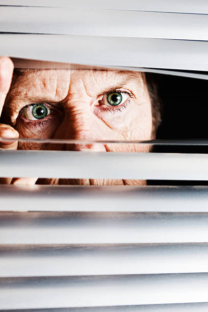 istock Irritated old woman looks though blinds angrily 155287584