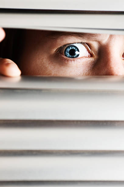istock Close up of nervous woman's eye looking through blinds 155287713