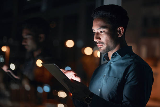 istock Night, work or man reading on tablet for research, project or planning a proposal in office building, startup or professional employee. Overtime, working or search on internet or online communication 1552877778