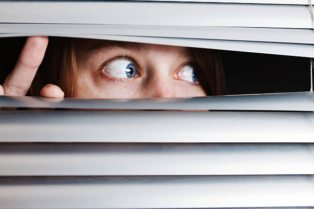 istock Young woman is terrified by something seen through venetian blinds 155287795