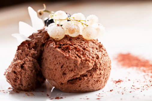 chocolate mousse dessert on a plate with garnish of black and white currant, white currant covered with sugar, cocoa powder used for decoration