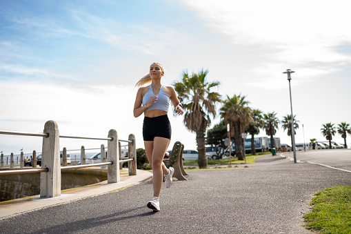 Sporty young woman in fitness clothing running on a promenade in summer