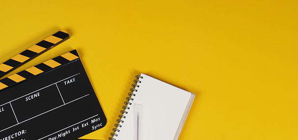 Yellow Clapper board with notebook and pens on yellow background.