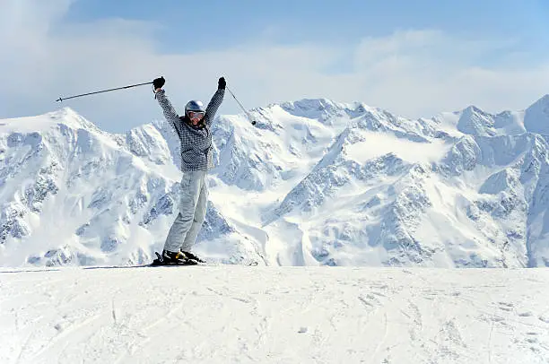 female skier happily rising her hands up at mountain range background