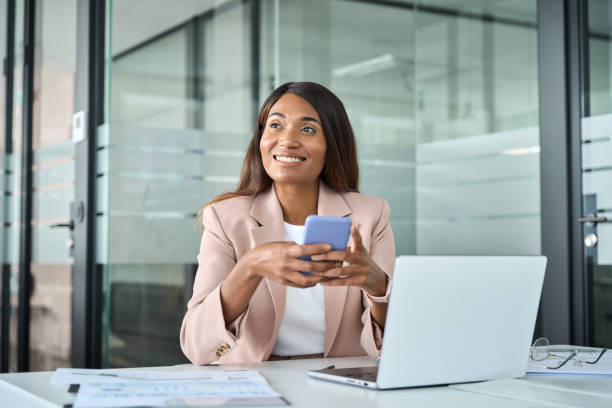 istock Happy professional business woman using mobile phone looking away in office. 1552918835