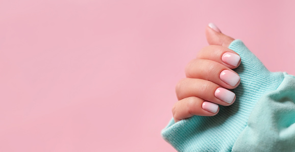 Gradient manicure and Hands Spa. Banner with copy space for text. Beautiful Woman hand closeup. Manicured nails and Soft hands skin. Beautiful woman's nails with beautiful baby boomer manicure, pink background.
