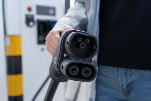 istock Woman holding fast charging socket type 2 plug for electric vehicles at EV car charging station. 1552952632