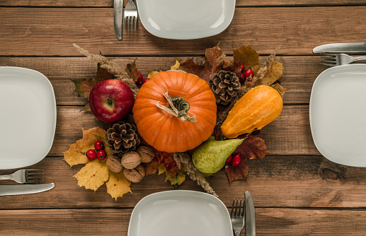 Thanksgiving dinner table wooden table. Autumn or fall flat lay composition. Four plates and cutlery, with decorative pumpkins, cones, apple, pear, nuts, rosehips and leaves in the middle.