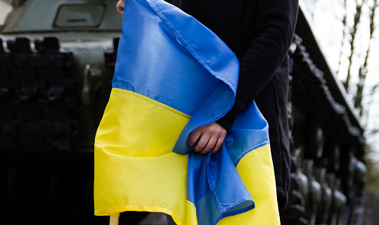 Mujer sosteniendo la bandera ucraniana, junto a un tanque de batalla. Guerra en Ucrania, concepto de crisis. photo