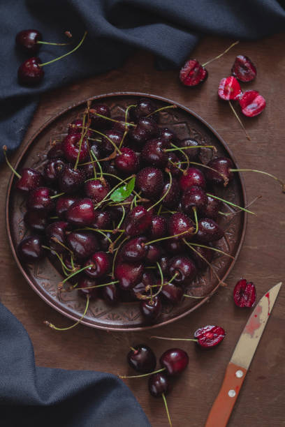 istock Fresh red cherry in a flat ceramic plate on a wooden background. Top view. 1552975879