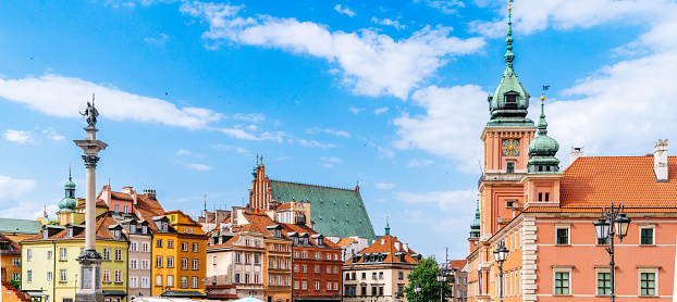 A clear view of the architectural ensemble surrounding Plac Zamkowy, also known as Castle Square, in Warsaw's Old Town Centre. The frame captures the various buildings in the area, including the notable Warsaw Castle. On the left side of the image, Kolumna Zygmunta III Wazy, or Sigismund's Column, is visible, adding a historical element to the scene. The focus of the photograph is solely on the buildings, devoid of any people or visible roads. The blue sky above showcases scattered clouds, completing the view of this historic urban landscape.