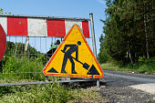 Road work ahead warning sign on a fence of construction site of new road. Roadworks traffic sign in Poland.