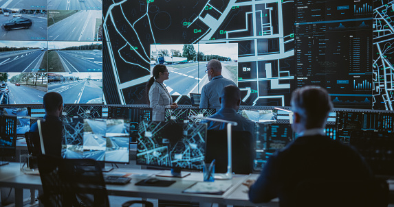 Futuristic City Logistics Planning Monitoring Center with Diverse Male and Female Officers Analyzing Live CCTV Footage on a Big Digital Screen. Talented Team of Specialists Working in Office